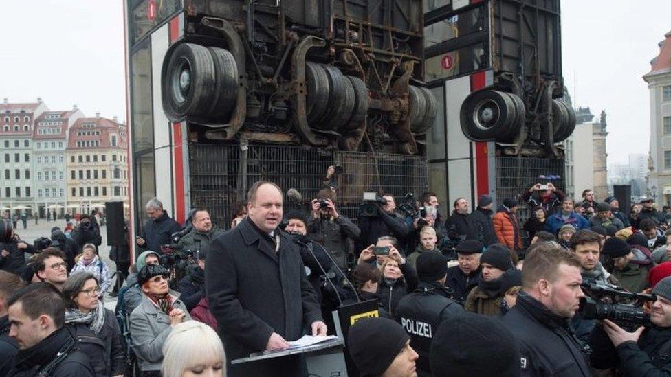 Police stand around Dresden's Mayor Dirk Hilbert (centre) as he gives a speech in front of the busses sculpture (07 February 2017)