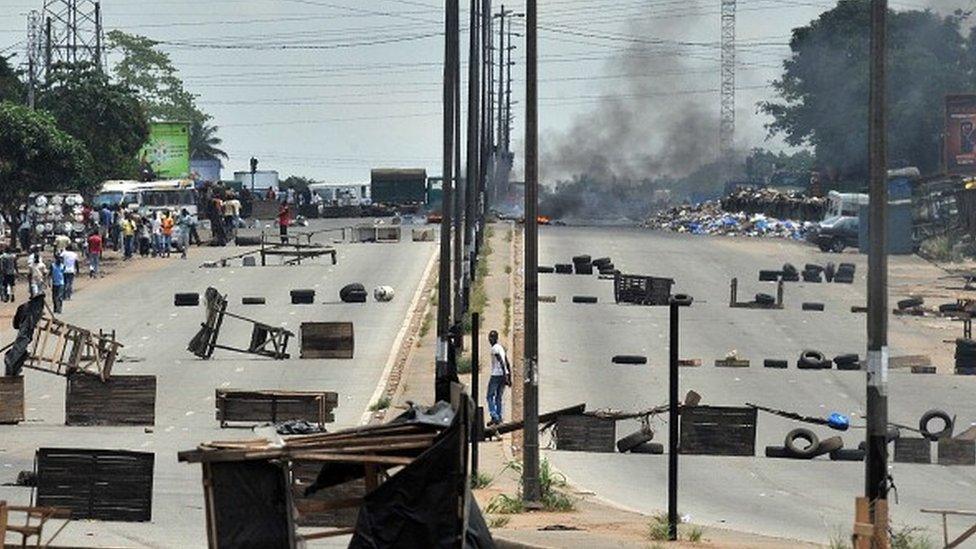 Residents walk past barricades and burning tires on the main road leading to the Abobo district of Abidjan on March 15, 2011