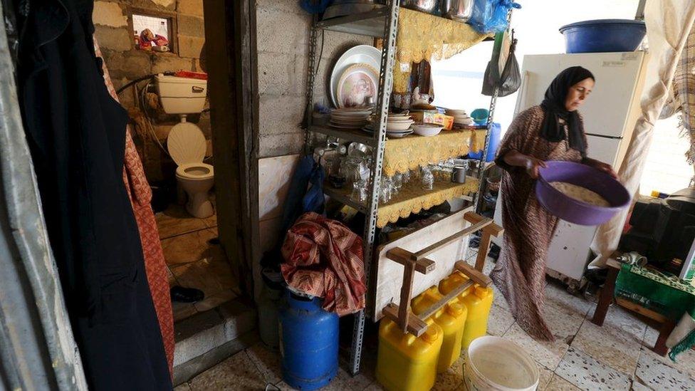 A woman passes near the entrance to a toilet in a makeshift shelter used by a Palestinian family in Khan Younis, in the southern Gaza Strip
