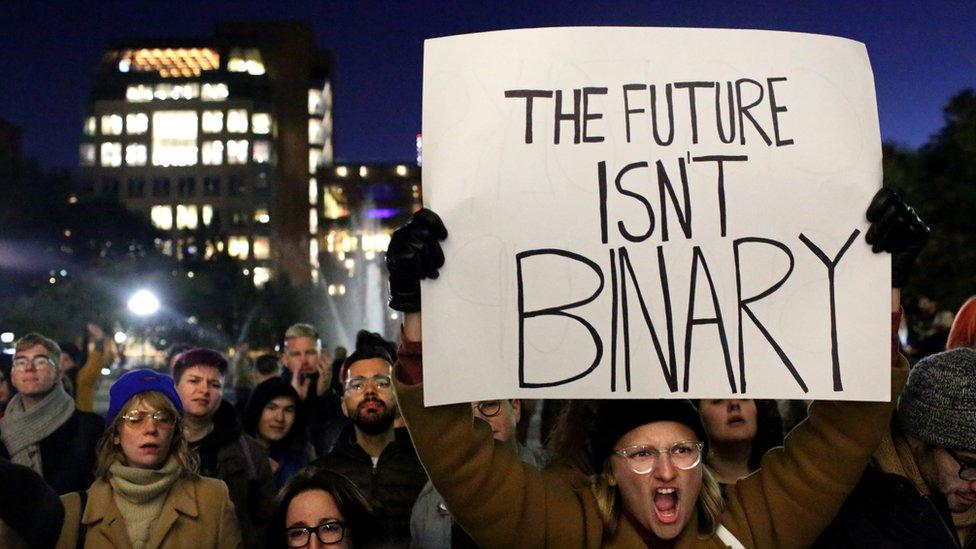 Protesters in New York. One holds a sign saying 'The future isn't binary'