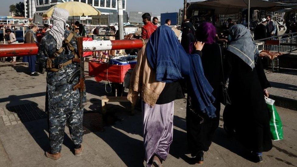 Women walk past a Taliban guard