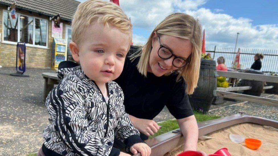 A mum and her young son playing together with toys in a sandbox