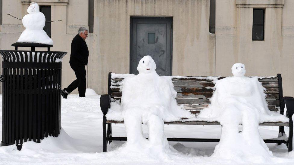 Snowy men spring up on a park bench