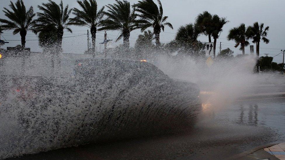 A car drives down a flooded street ahead of Hurricane Nicole hitting