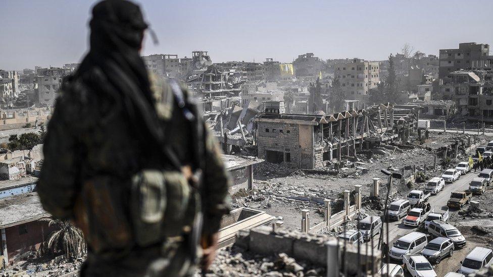 A fighter of the Syrian Democratic Forces stands guard on a rooftop in Raqqa after retaking the city from Islamic State