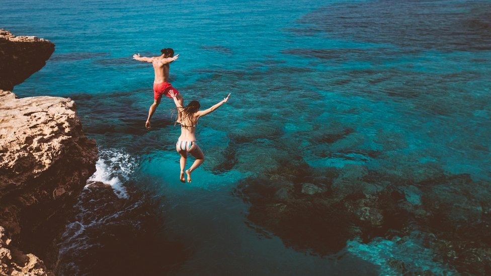 A couple jumping into beautiful blue water