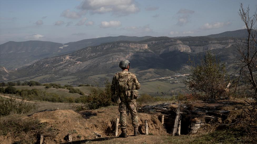 An Azerbaijani soldier in front of a burned stretch of trench at a retaken Armenian outpost.