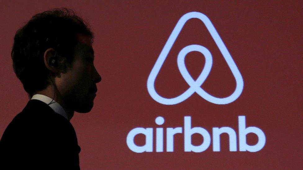 A man walks past a logo of Airbnb