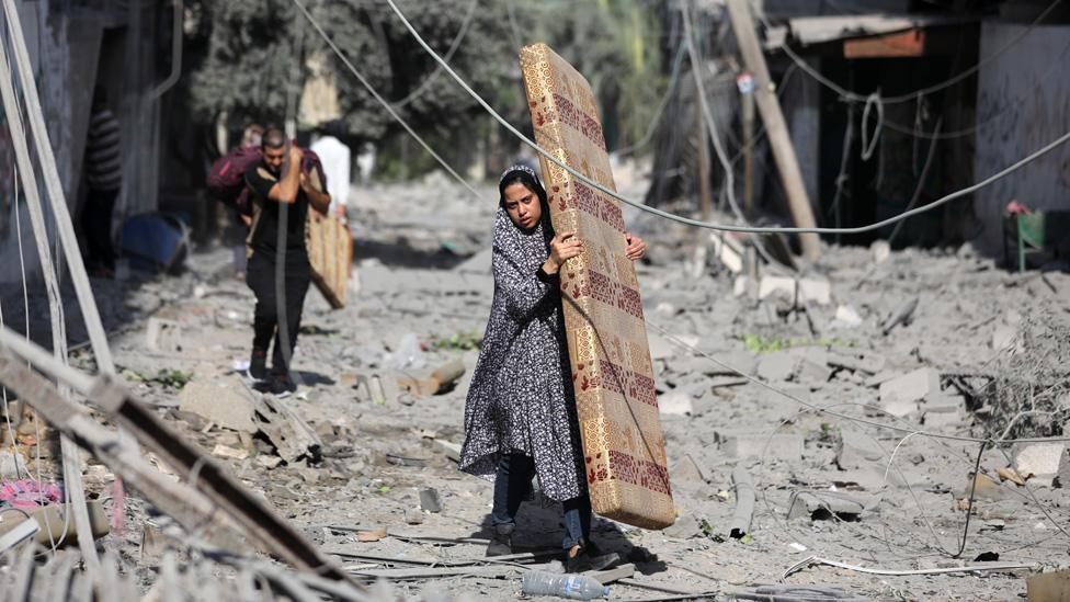 Palestinians walk through debris along a street in the aftermath of Israeli bombardment in al-Karama district in Gaza City