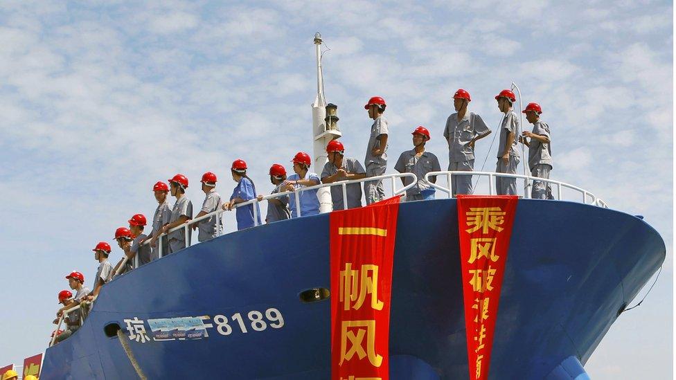 Uniformed staff in red helmets, standing on a fishing vessel setting sail for the Spratly Islands, draped with red and yellow flags on which are written slogans in Chinese, on 6 May 2013.