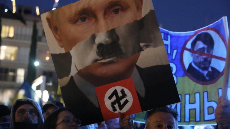 People hold placards as they watch Ukrainian President Volodymyr Zelensky speech broadcasted live at Habima square in Tel Aviv, Israel