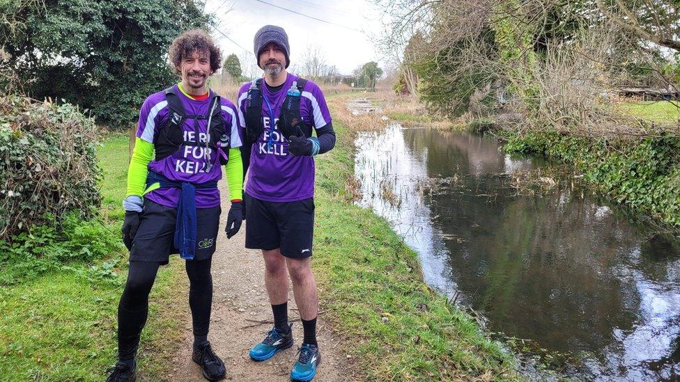 John Fielding (left) and Michael Pendry (right) standing by a lake wearing purple running gear