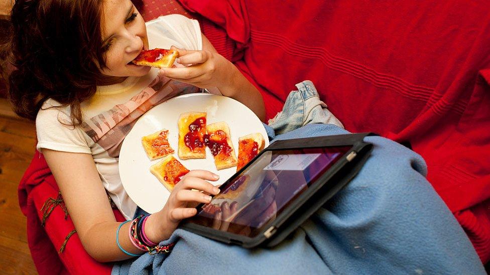 young girl eating toast and looking at her tablet