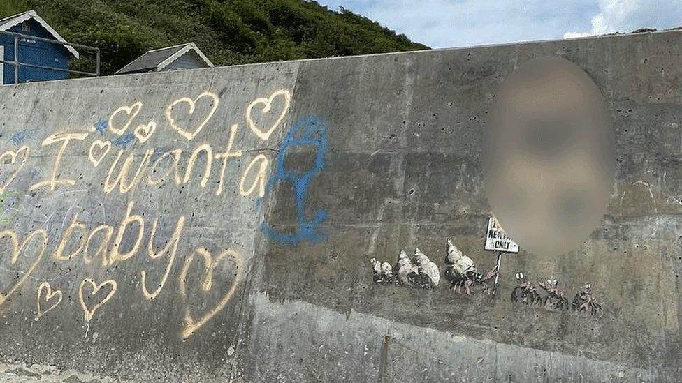 Graffiti on sea wall at Cromer, including 'I want a baby' and hearts in spray paint, with some spraypaint on part of the Banksy mural