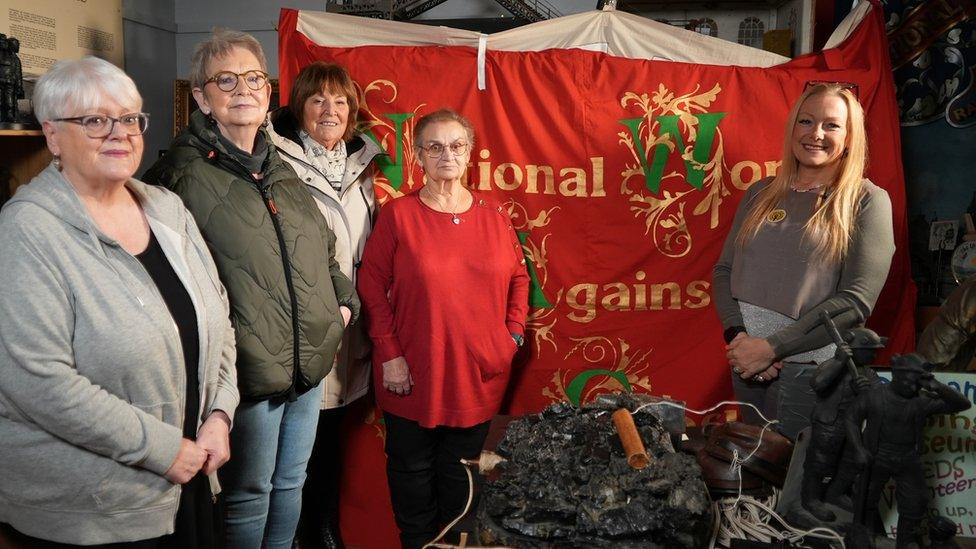 Five women stand in front of a large red miners' union banner