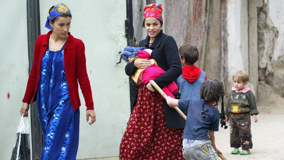 A Tajik girl cleans a rug as two women pass by her in Dushanbe, 23 October 2006