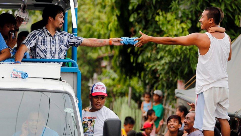 Filipino boxing champion and senate candidate Emmanuel "Manny" Pacquiao, riding on the top of an election vehicle, hands a rolled up blue election shirt to a villager holding a child during a political campaign in the town of Bay, Laguna province on 28 April 2016