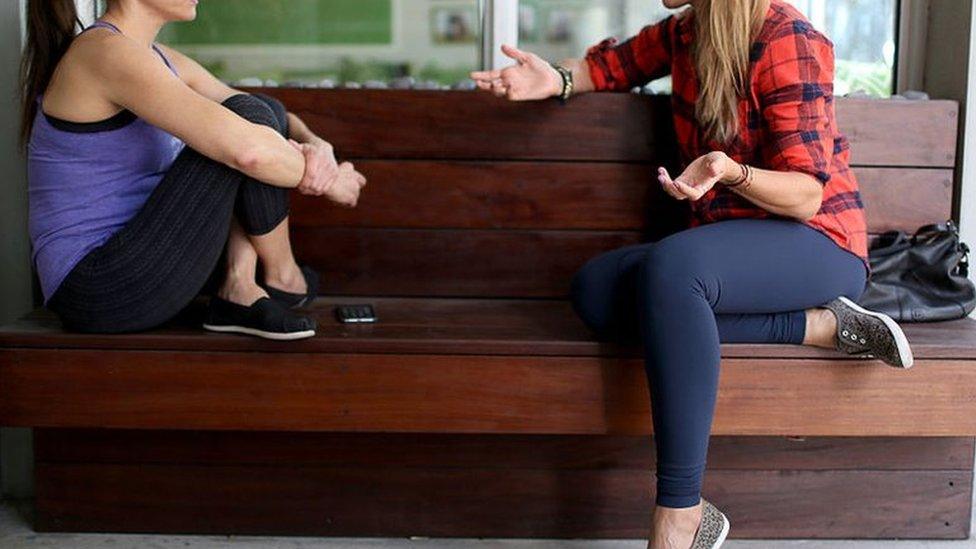 Two women sit on a bench, wearing yoga pants