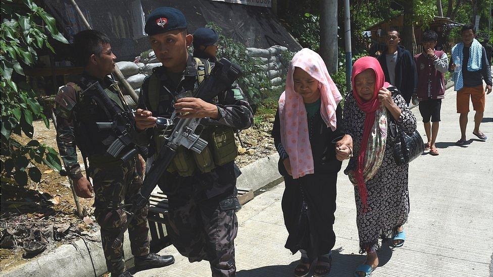 Philippine policemen walk with evacuees from Marawi at a checkpoint on the southern Philippines island of Mindanao