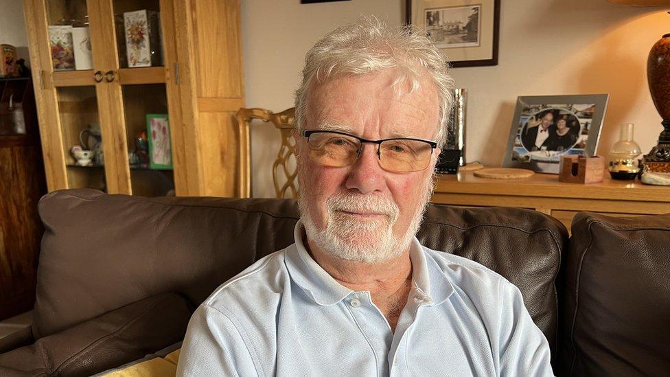 Man with beard and glasses sits on leather sofa and looks at camera