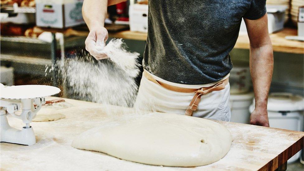 Baker sprinkles flour on dough