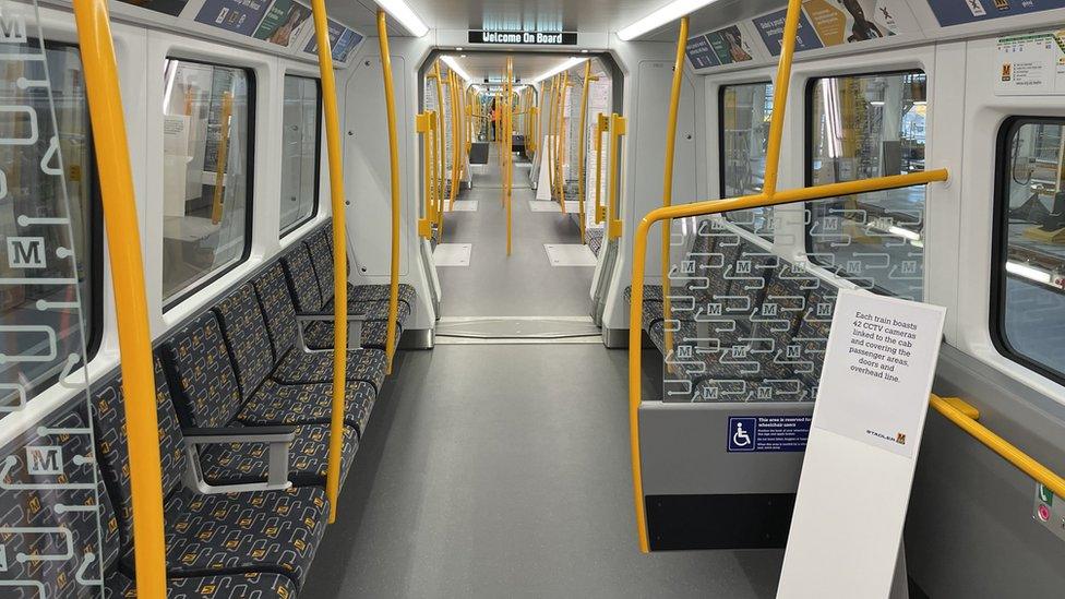 Interior of train showing grey and yellow seats down the sides of the carriages