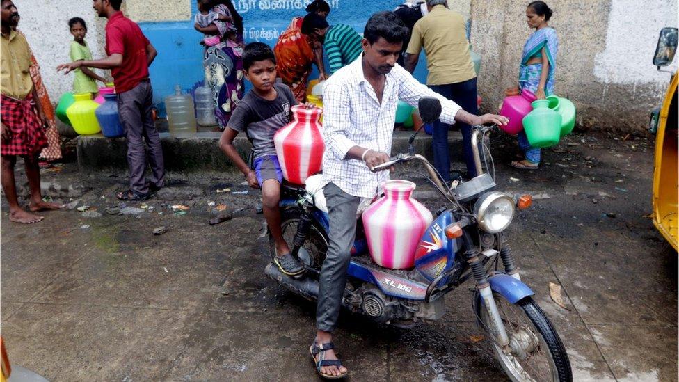 An Indian man with kid arranges plastic vessels filled with drinking water on his scooter at a water distribution point, which are replenished by water tankers, in Chennai, capital of the southern Indian state of Tamil Nadu, Wednesday, June 20, 2019.