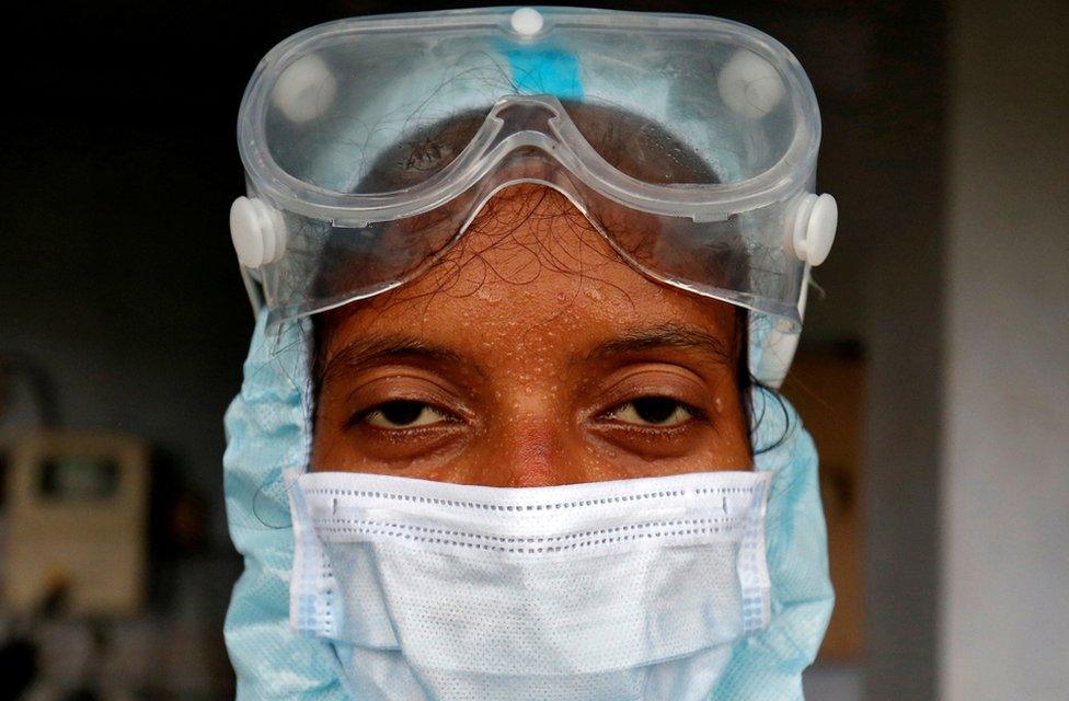 Beads of sweat run down the forehead of a healthcare worker wearing protective gear