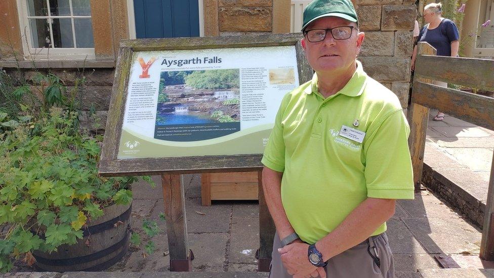 Image of a volunteer standing beside an information sign