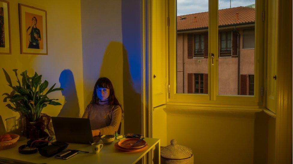 Lucia is seen sitting alone in her apartment, using a laptop at a table