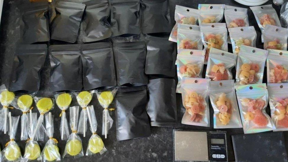 Yellow cannabis lollies and bags of red and orange cannabis sweets laid out on a counter