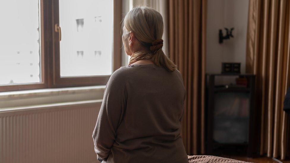 Senior woman sitting on bed and looking out of the window