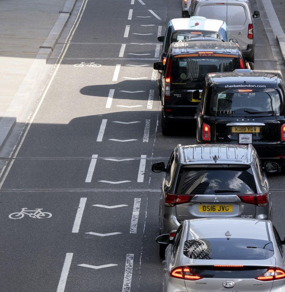 Alongside an empty cycle lane, queues of traffic wait for a green light on London Wall in the City of London