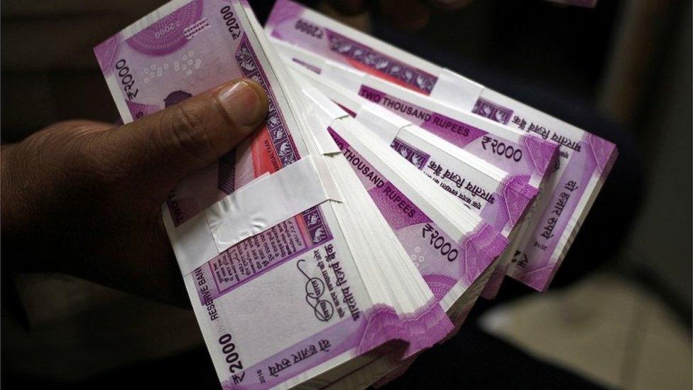 A bank worker holds wads of Indian rupee banknotes