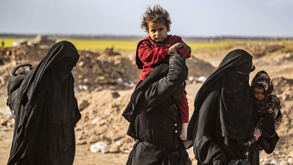 Fully-veiled women carry their children after being evacuated from the last IS-held territory in the eastern Syrian village of Baghuz (6 March 2018)