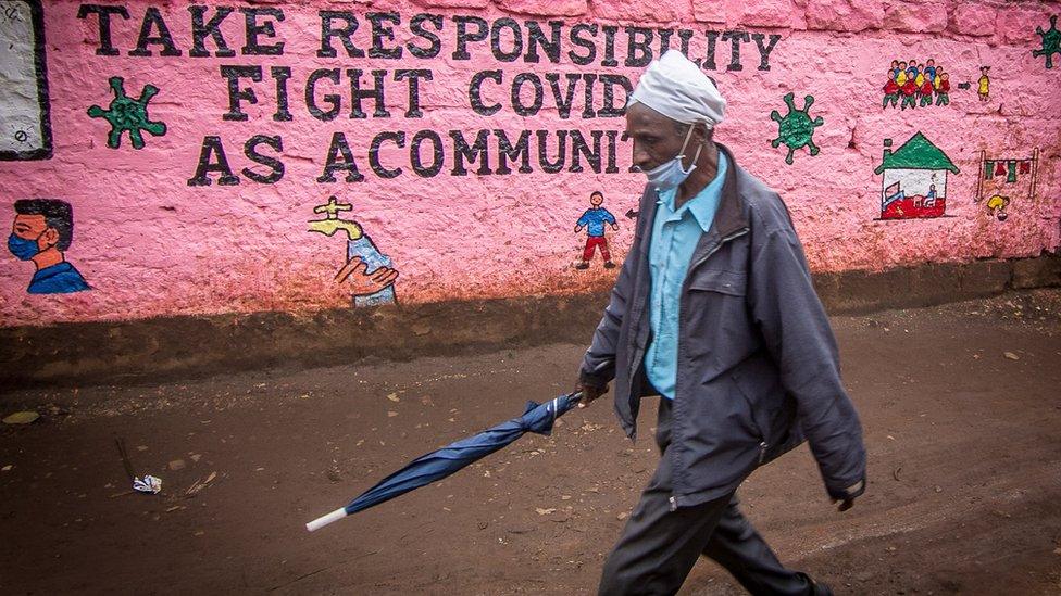 A man wearing a face mask as a precaution, walks past a wall with an awareness graffiti during the corona virus pandemic