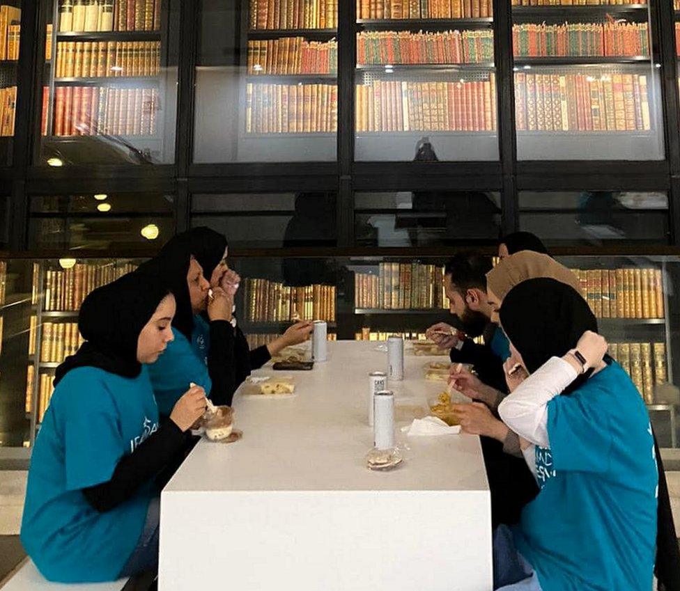 volunteers take time out to eat in front of a massive book display at the British Library