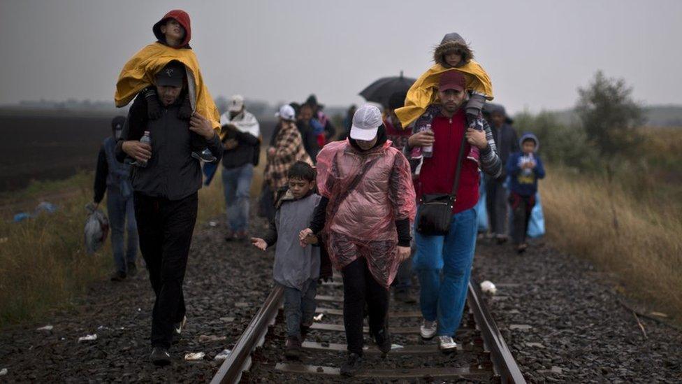 Syrian refugees walk along a train track