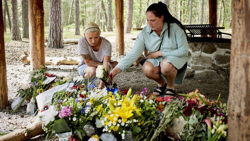 People lay flower bouquets as a makeshift memorial at a forest shelter next to the Haslevej road near Roenne, Bornholm island, Denmark,