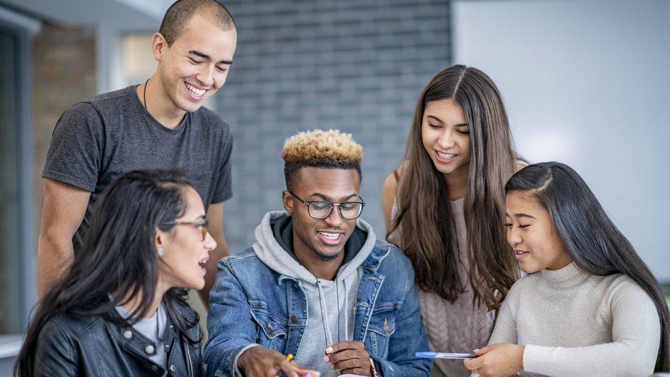 A diverse group of students discuss the study material on the table in front of them.