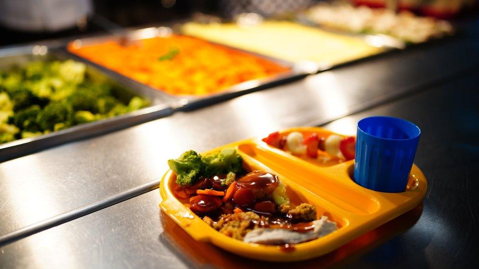 A school meal tray containing mashed potatoes, broccoli, a fruit skewer and a blue cup