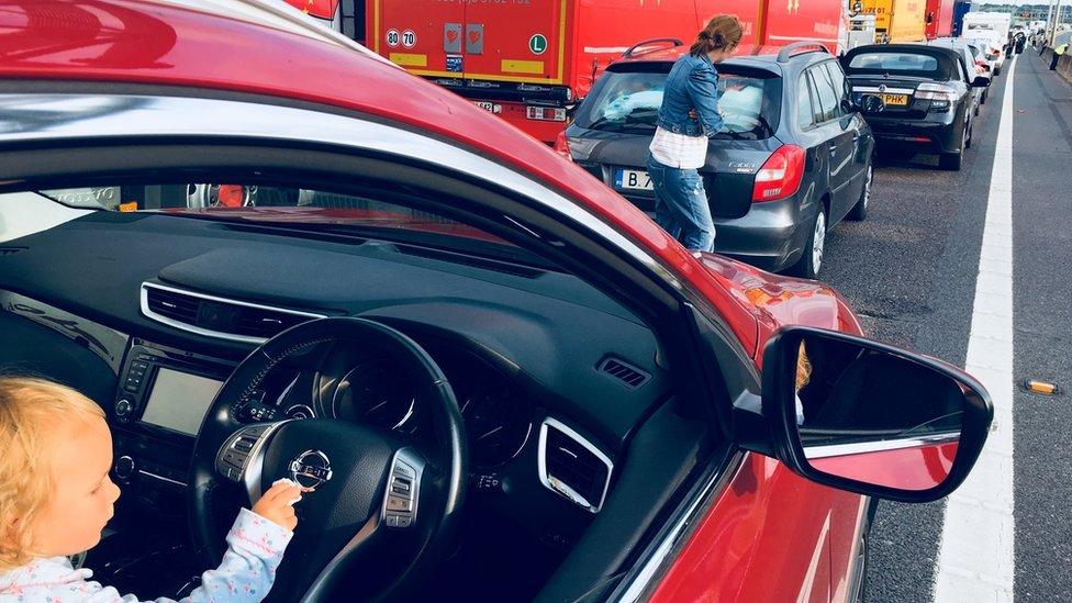 Two-year-old girl sitting in the driver's seat of a car in a traffic jam