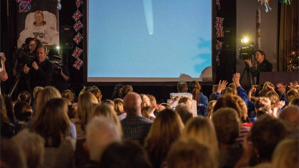 People gathered in a hall watching a space launch on a big screen