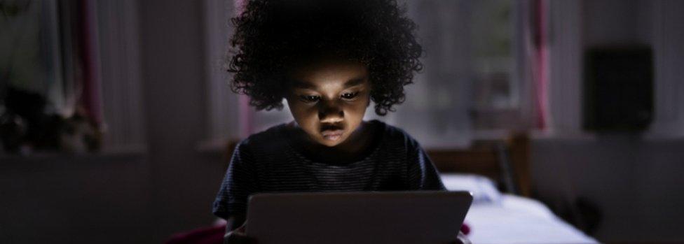 Child surfing internet on a computer tablet in his bedroom