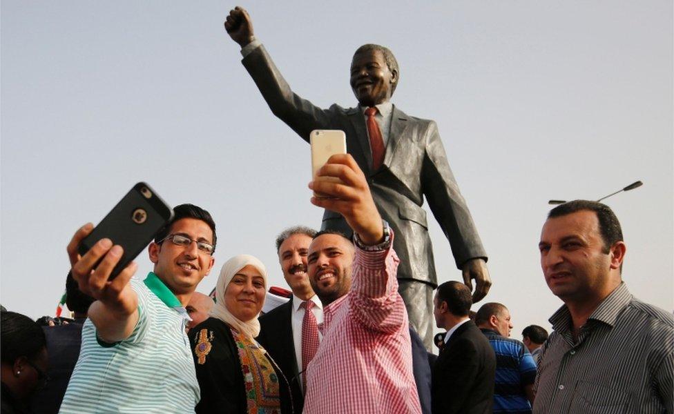Palestinians take selfies in front of a giant statue of Nelson Mandela following its inauguration ceremony in the West Bank city of Ramallah on April 26, 2016.