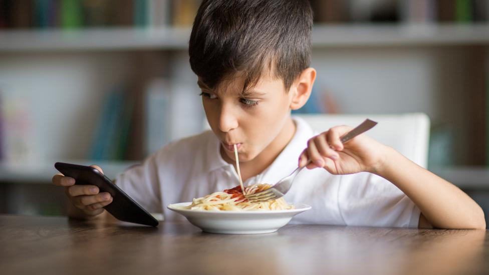 Boy eating and looking at a mobile phone