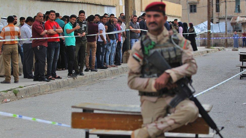 Members of the Iraqi security forces stand guard as people queue at a polling station in Mosul, 12 May 2018