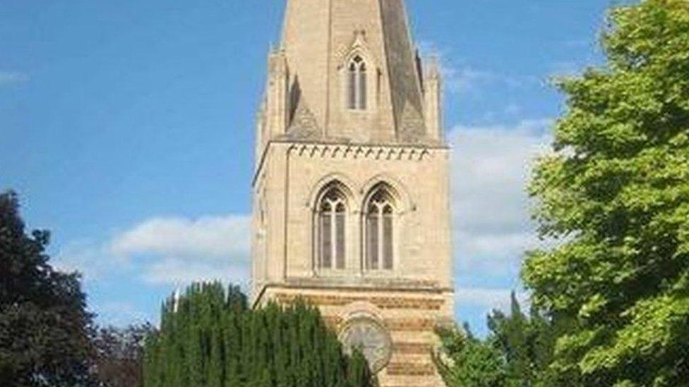 Part of the tower of a church, showing two arched windows. Trees in foreground