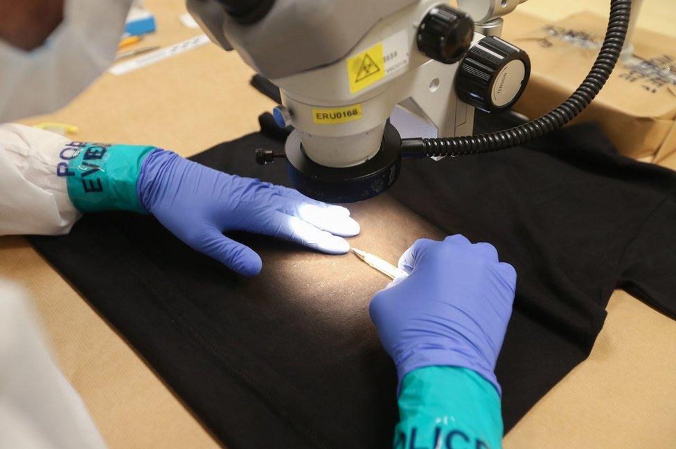 A forensic examiner uses a pen to gauge scale, using the traditional method of blood detection