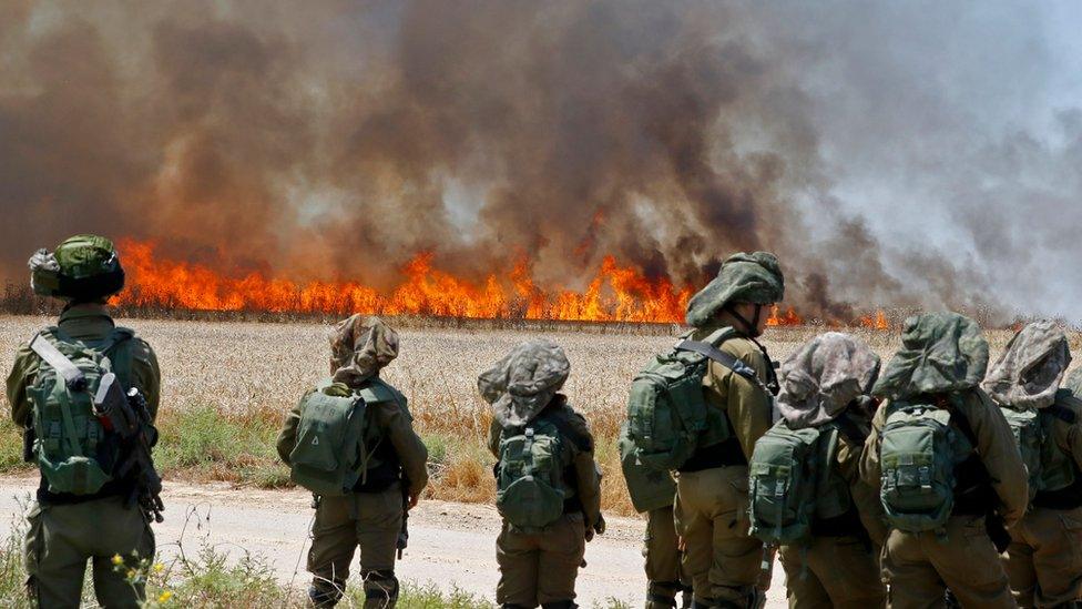 Israeli soldiers walk amidst smoke from a fire in a wheat field near the Kibbutz of Nahal Oz, along the border with the Gaza Strip, on May 14, 2018